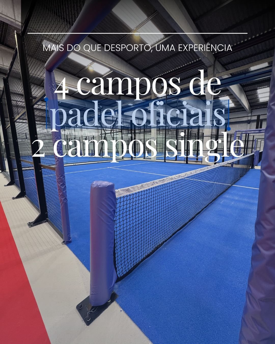 Quadra de padel com piso azul e traves de proteção preta, localizada em ginásio com teto de ferro e iluminação artificial.